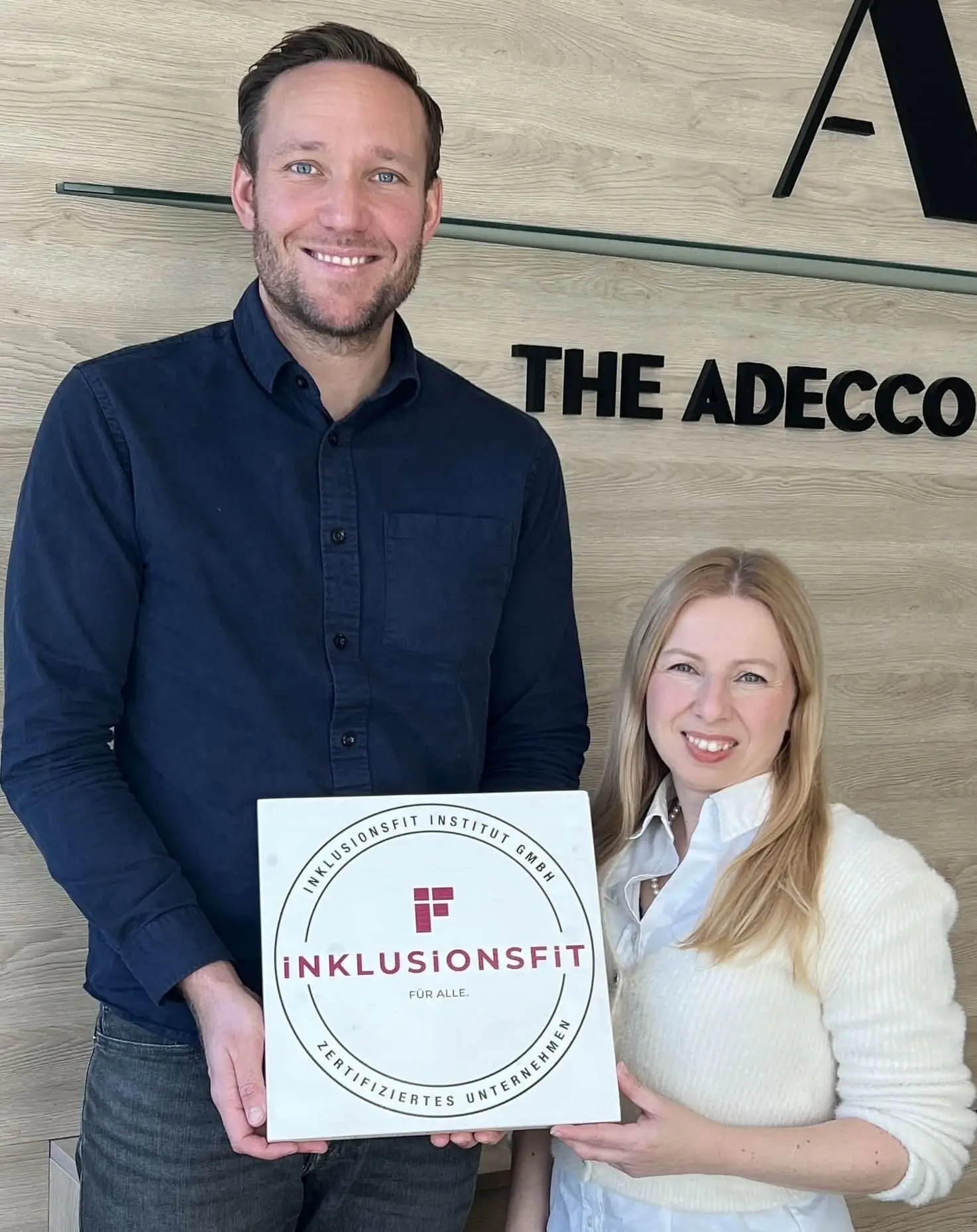 Nadine Schönwald von Adecco und Lars Hermes halten das Inklusionsfit Institut Siegel in die Kamera