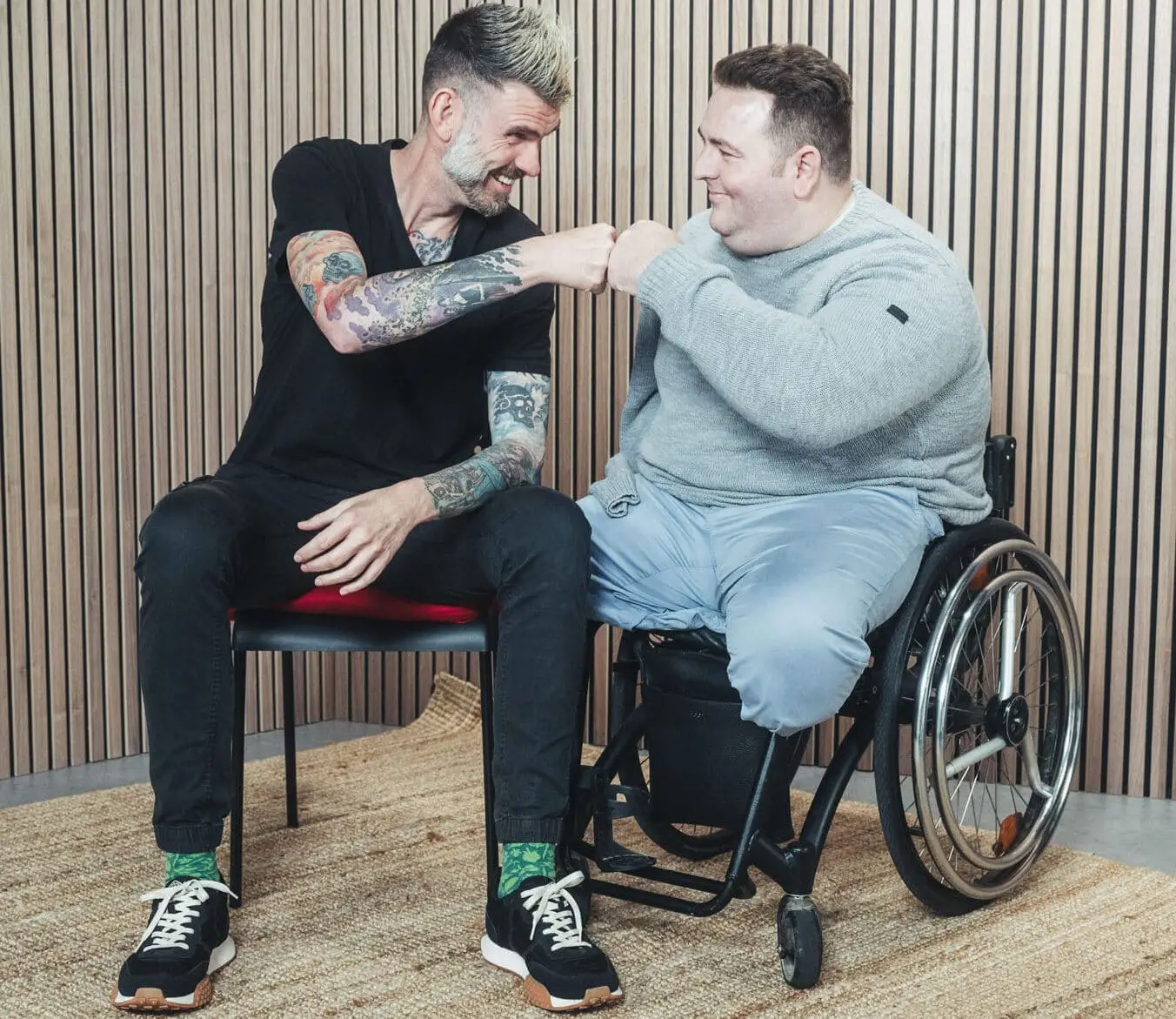 Rollstuhlfahrer Mirko und Fußgänger Martin sitzen auf einem Stuhl bzw. im Rollstuhl